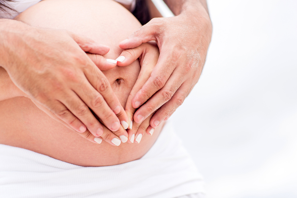 Pregnant couple with hands around belly making a heart shape